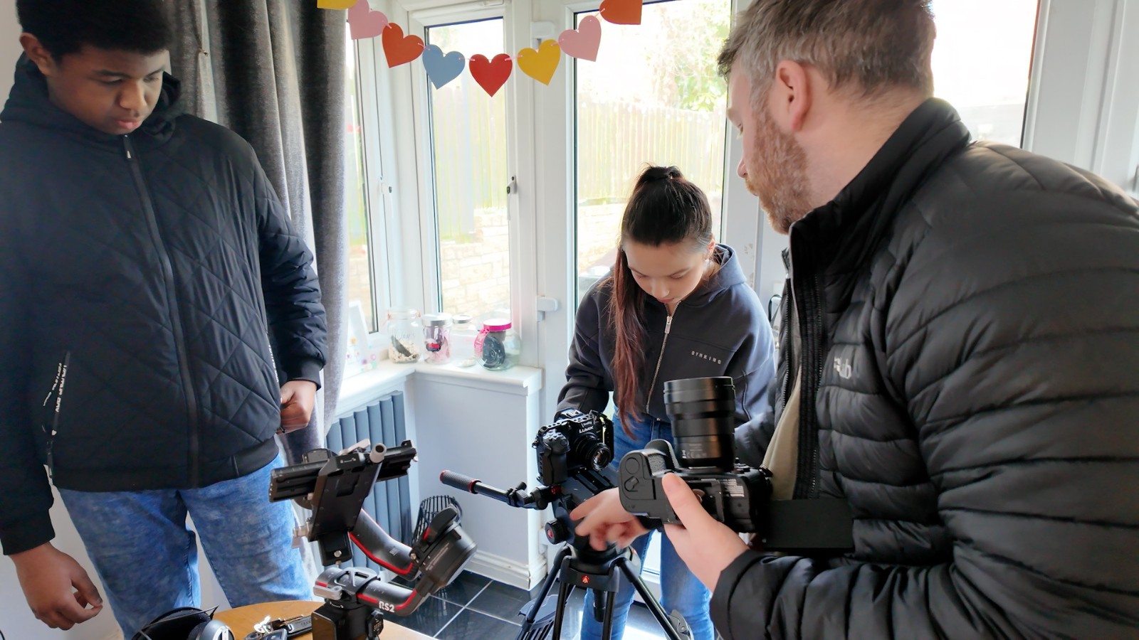 Three of the attendees of the Police Scotland Youth Volunteers screen education programme in Dunfermline. They are in a conservatory and hold camera equipment.