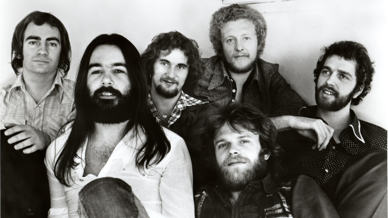Black and white image of the Scottish band, Average White Band, who sit in a row smiling at the camera