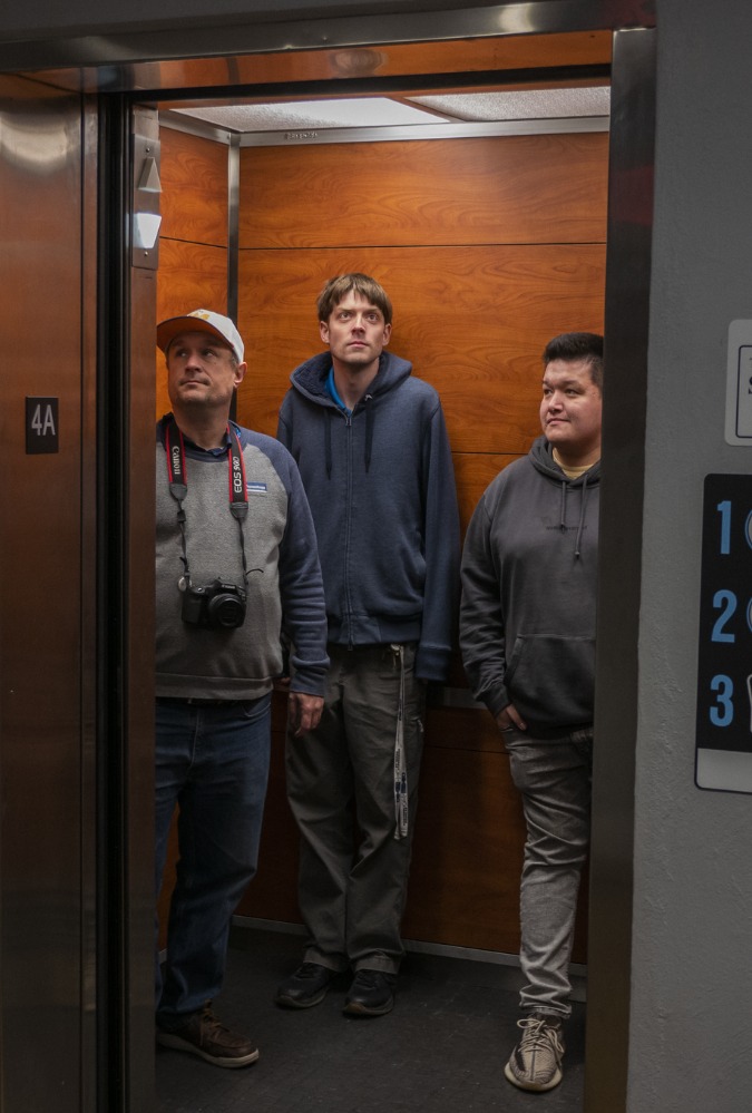 Still from documentary film Elevated, showing three men standing in an elevator which has its doors wide open