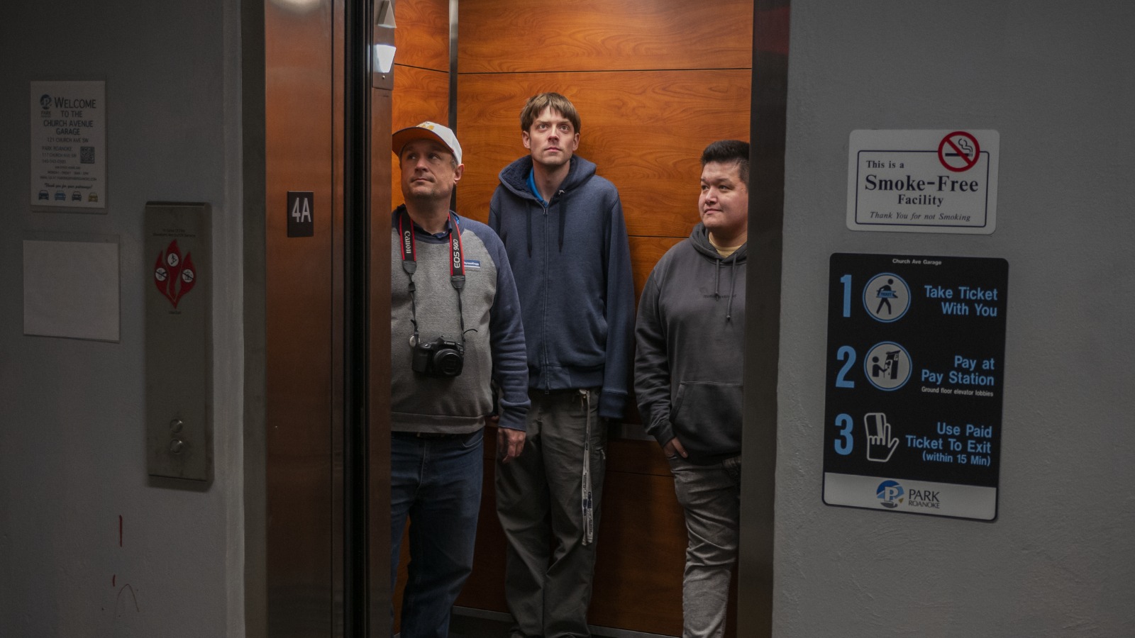 Still from documentary film Elevated, showing three men standing in an elevator which has its doors wide open