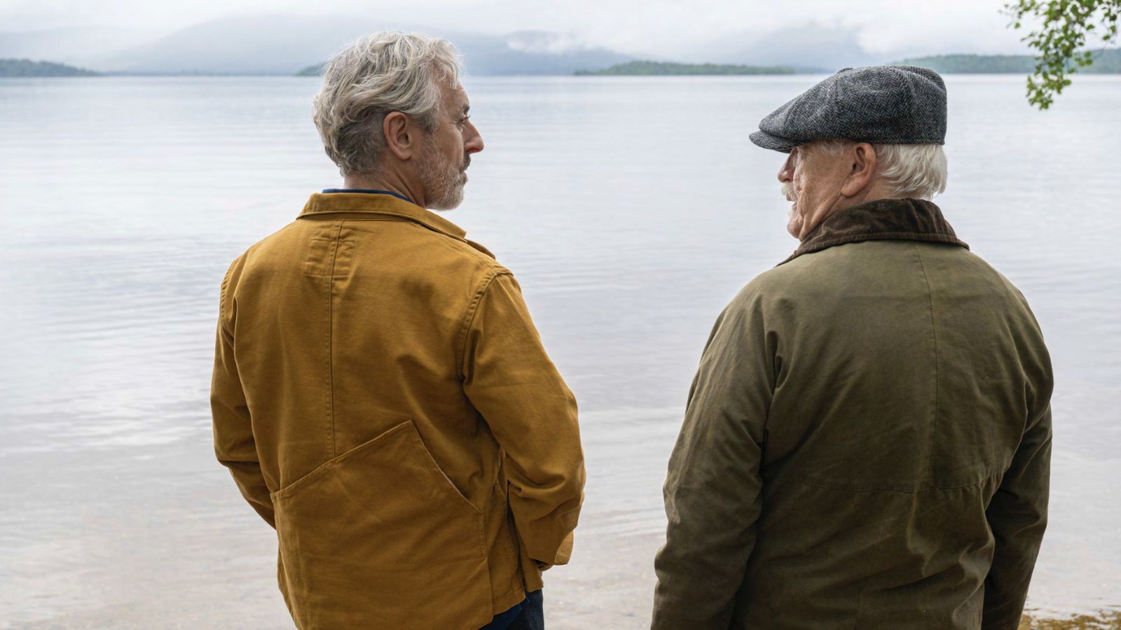 Still from Glenrothan, which shows actors Alan Cumming and Brian Cox standing side by side, looking at each other. They stand outdoors looking out over a loch.