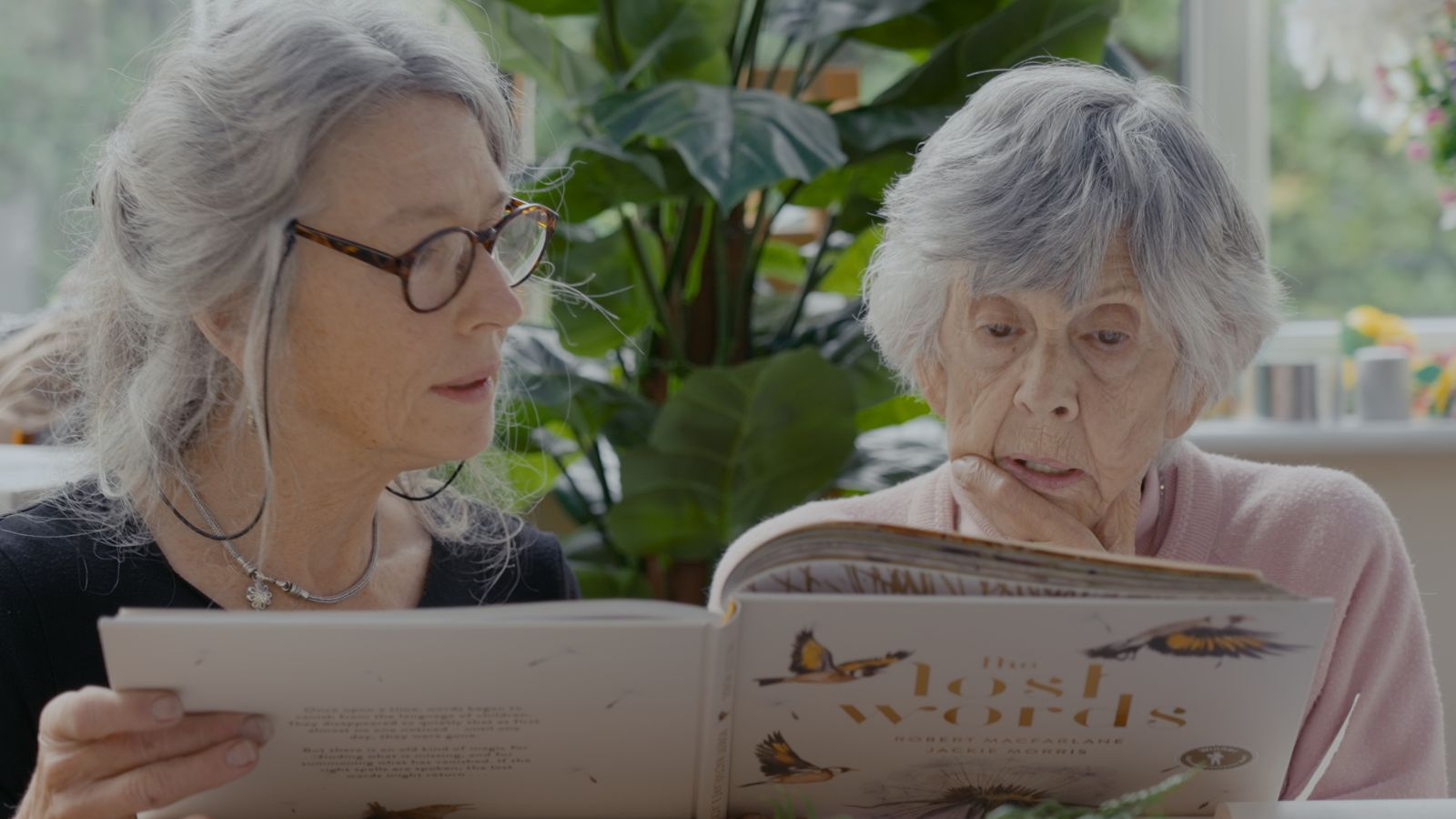 Still from Lost For Words showing two women sitting side by side at a table reading a book.