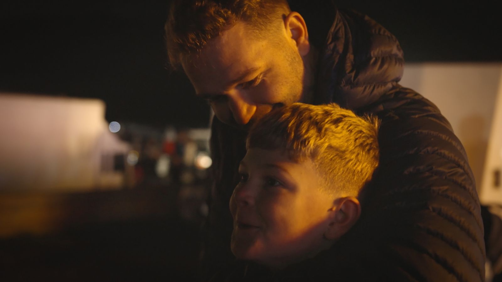 Still from Love and Trouble showing a man and a boy hugging. They stand outside and wear jackets.