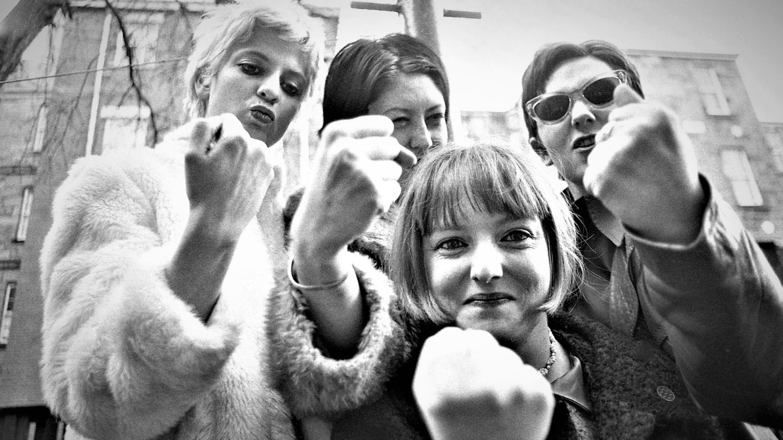 Black and white image of indie band Lung Leg. The four women stand and each hold up a fist up at the camera.