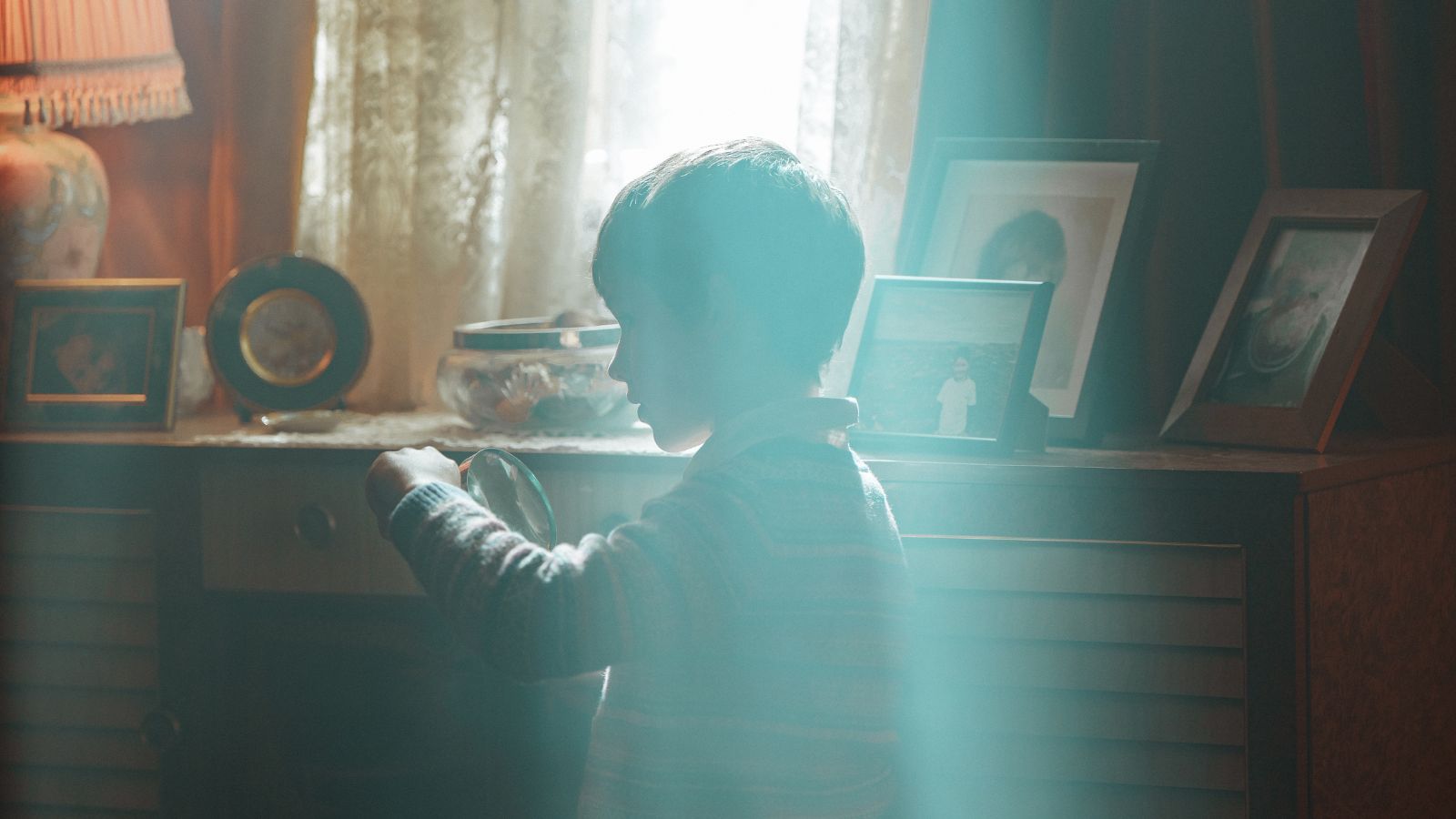 Still from Spilt Milk, showing a boy sitting at a desk, with light from the window behind him streaming in