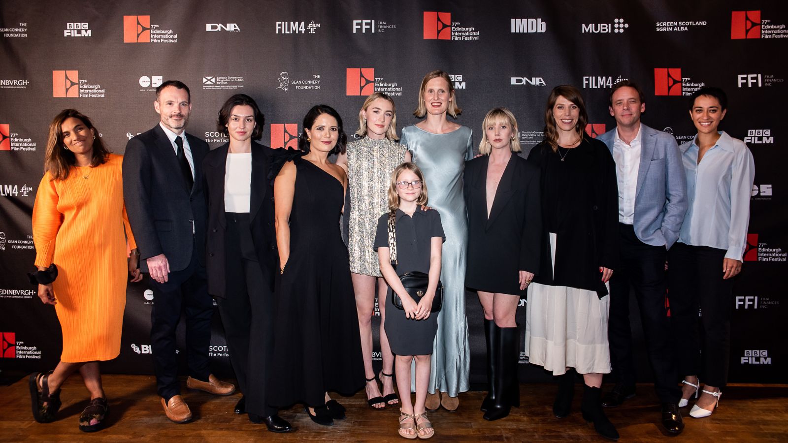 11 people stand in a line at the UK Premiere of The Outrun at the Cameo Cinema in Edinburgh, including actors Saoirse Ronan and Lauren Lyle, writer Amy Liptrot and director Nora Fingscheidt.