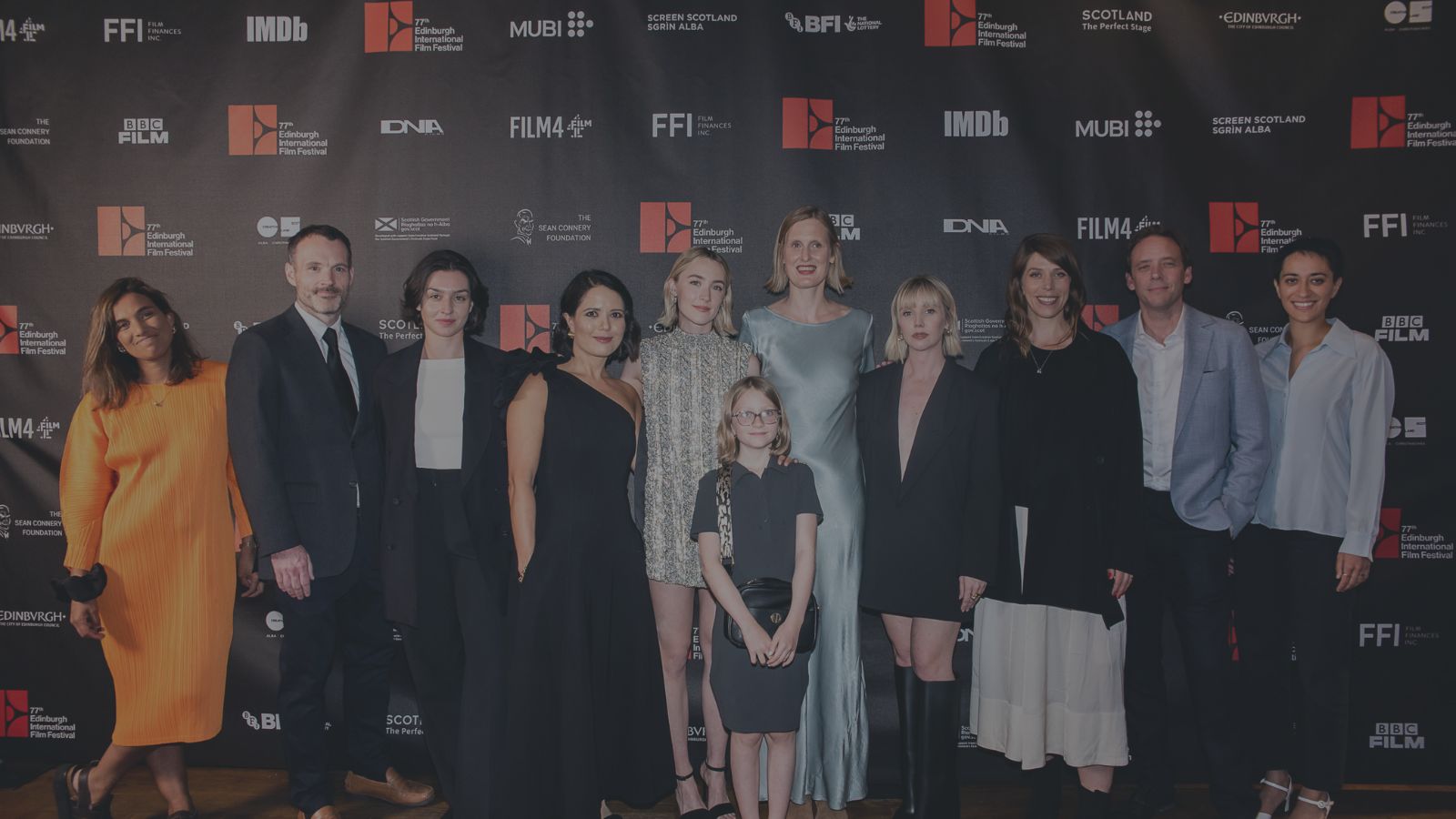 11 people stand in a line at the UK Premiere of The Outrun at the Cameo Cinema in Edinburgh, including actors Saoirse Ronan and Lauren Lyle, writer Amy Liptrot and director Nora Fingscheidt.