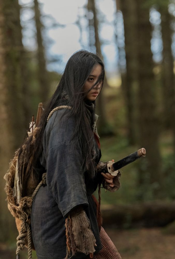 Still from Tornado, showing actor Koki standing outdoors in a wooded area. The wears clothing from the 1790s and holds a sheathed samurai sword.