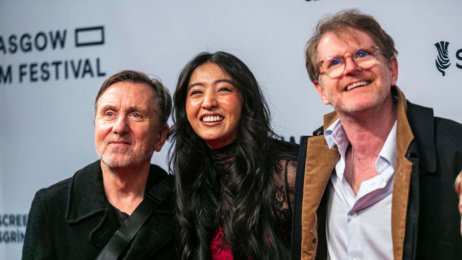 Tim Roth, Koki and John Maclean stand together on the red carpet smiling.