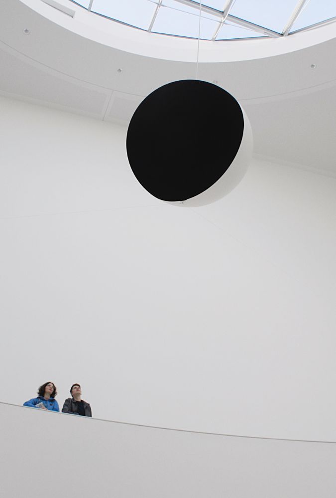 Still from Tracing Light. Two people stand in a gallery looking up at a an exhibit hanging from the ceiling.