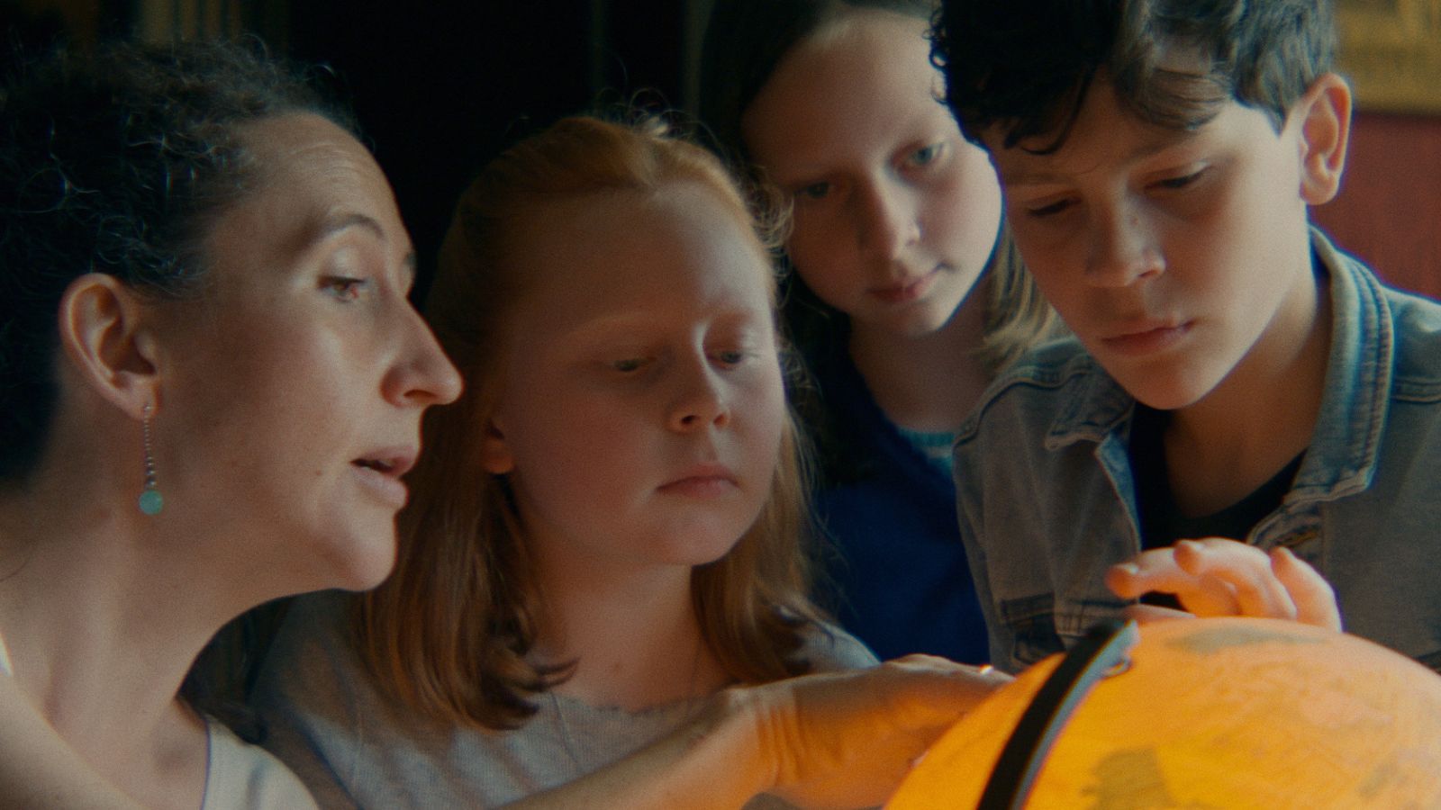 Still from Where Dragons Live, courtesy of Bombito Productions, showing an adult and three children in a row, looking closely at a lit up globe of the world.