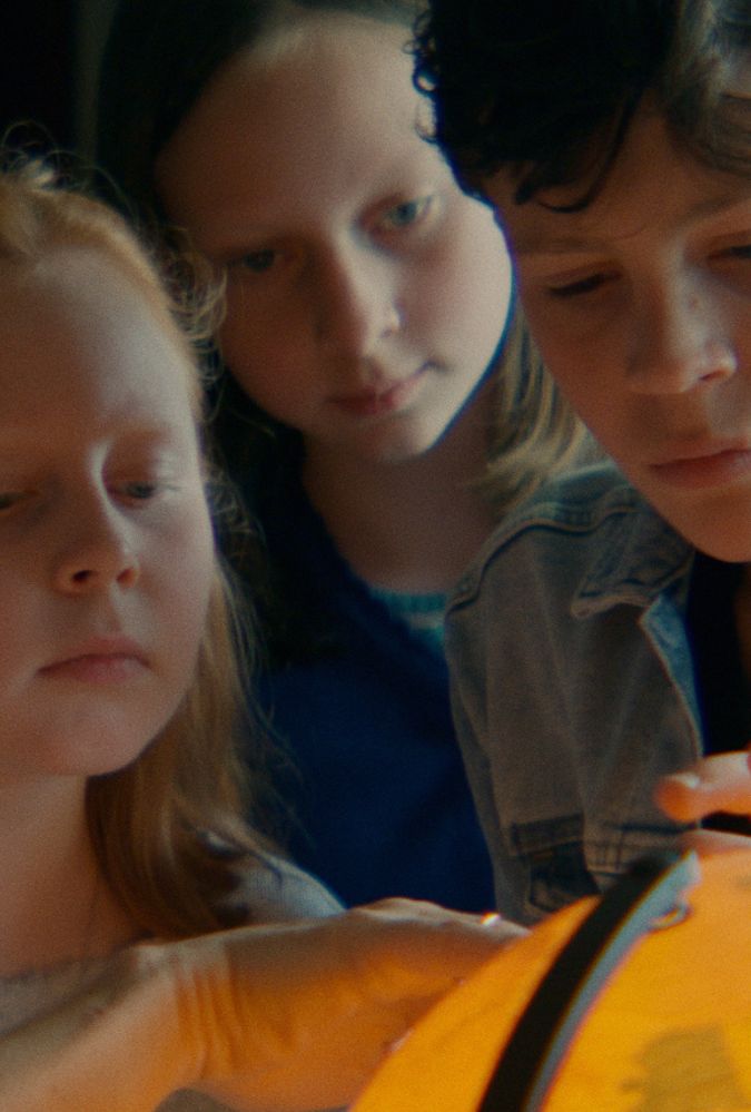 Still from Where Dragons Live, courtesy of Bombito Productions, showing three children in a row, looking closely at a lit up globe of the world.