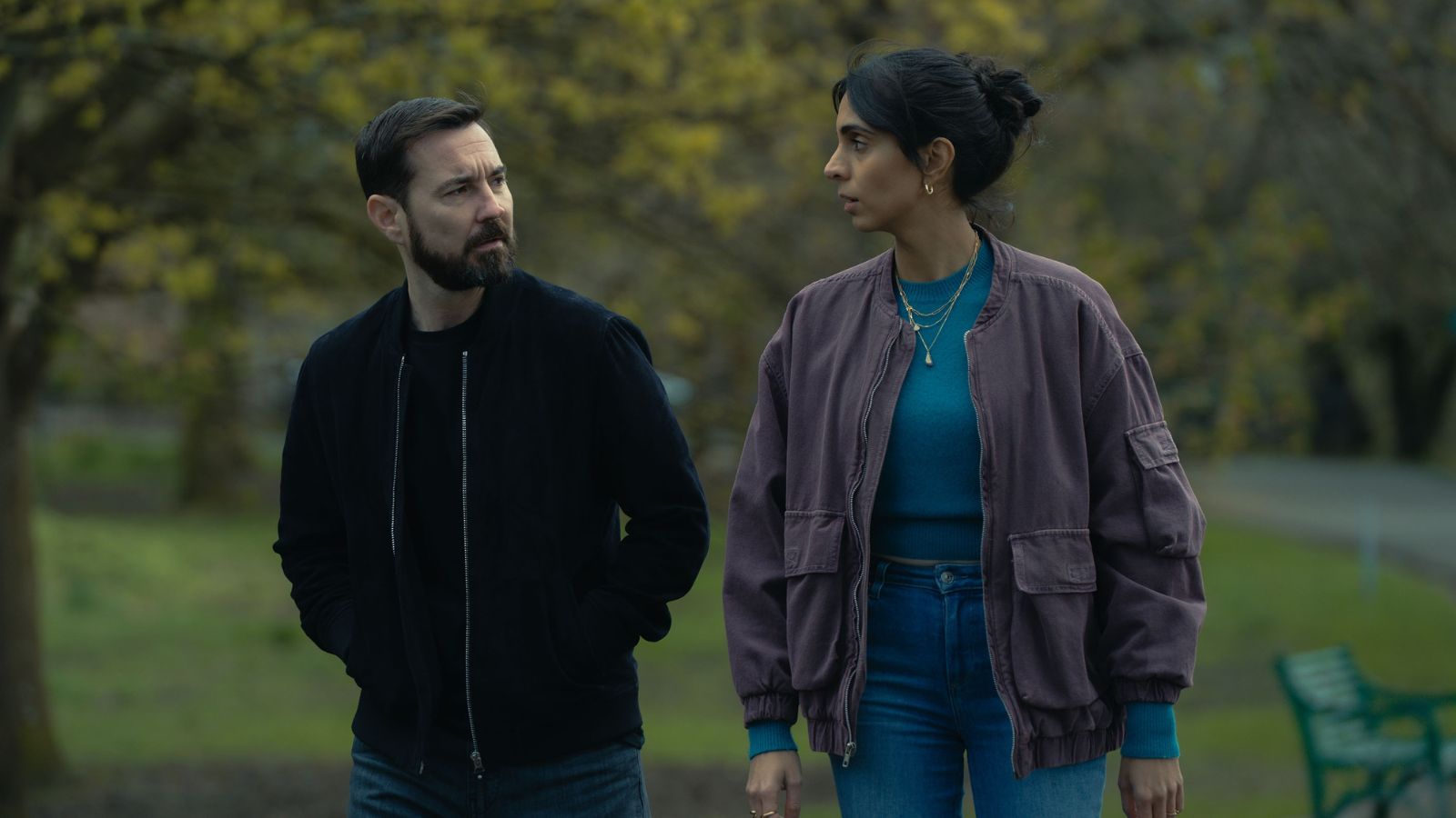 Still from Fear, courtesy of Prime Video. Actors Martin Compston and Anjli Mohindra walk side by side outdoors in a park in Glasgow.