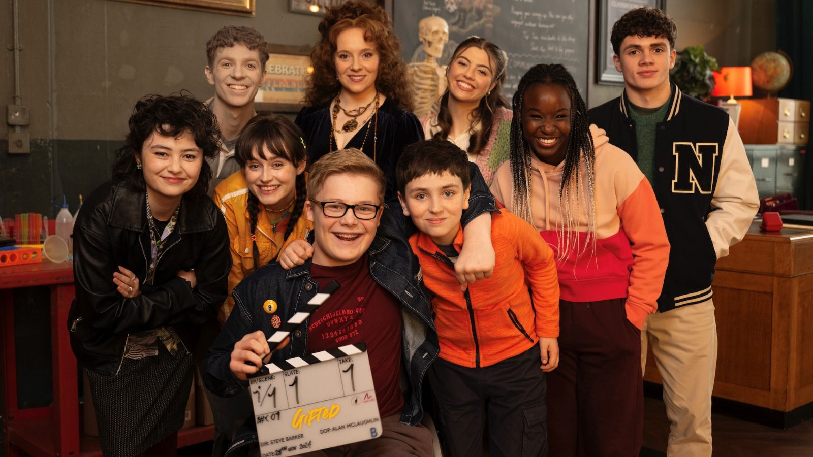 Promotional image from Gifted, which shows a group of teenagers standing together smiling at the camera. A boy in the centre holds a clapper board.