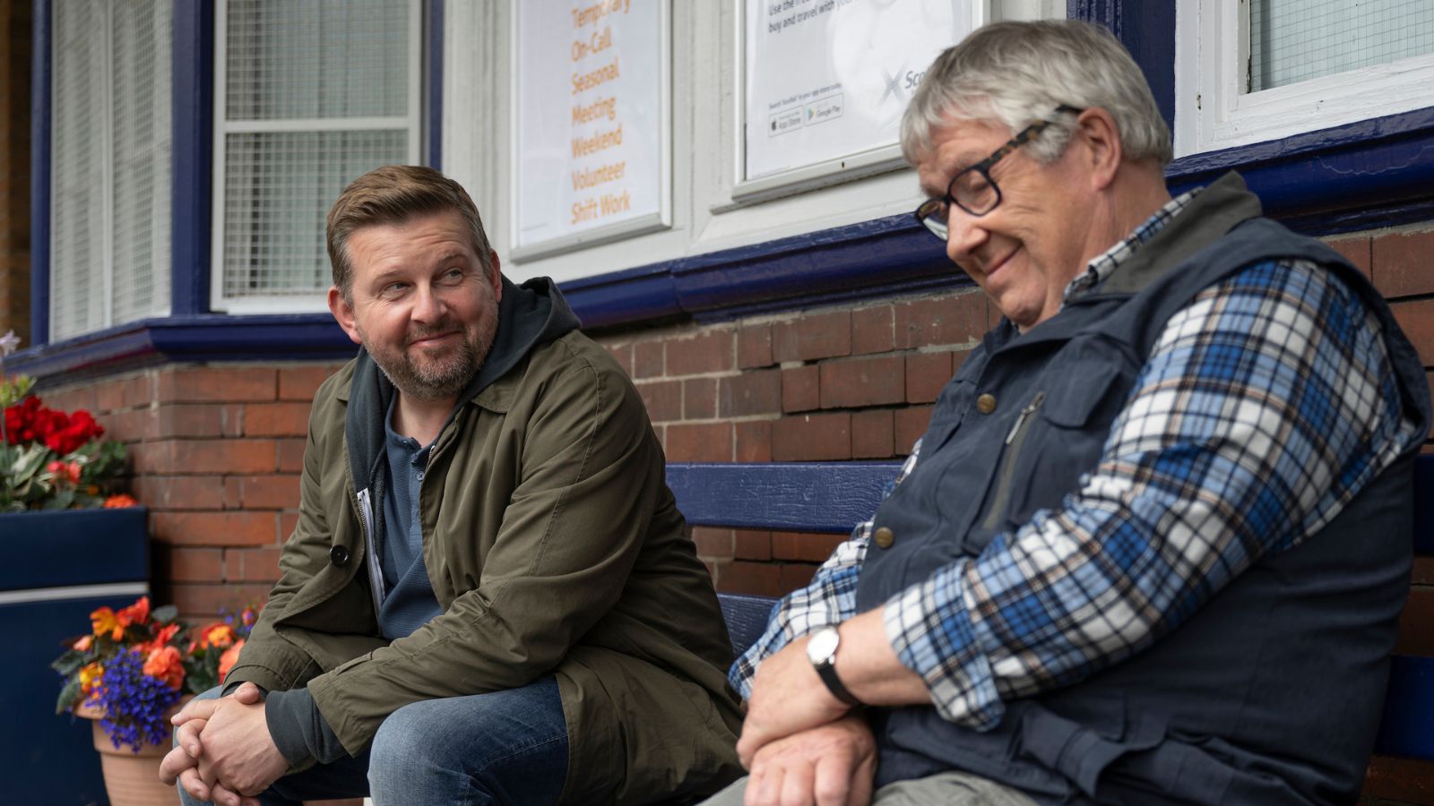 Still from Only Child, which shows actors Greg McHugh and Gregor Fisher sitting on a blue bench on a train station platform in Scotland.