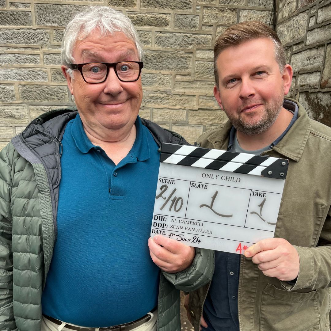 Gregor Fisher and Greg McHugh stand holding a clapper board, which is for Only Child. They stand outside in front of a brick wall.