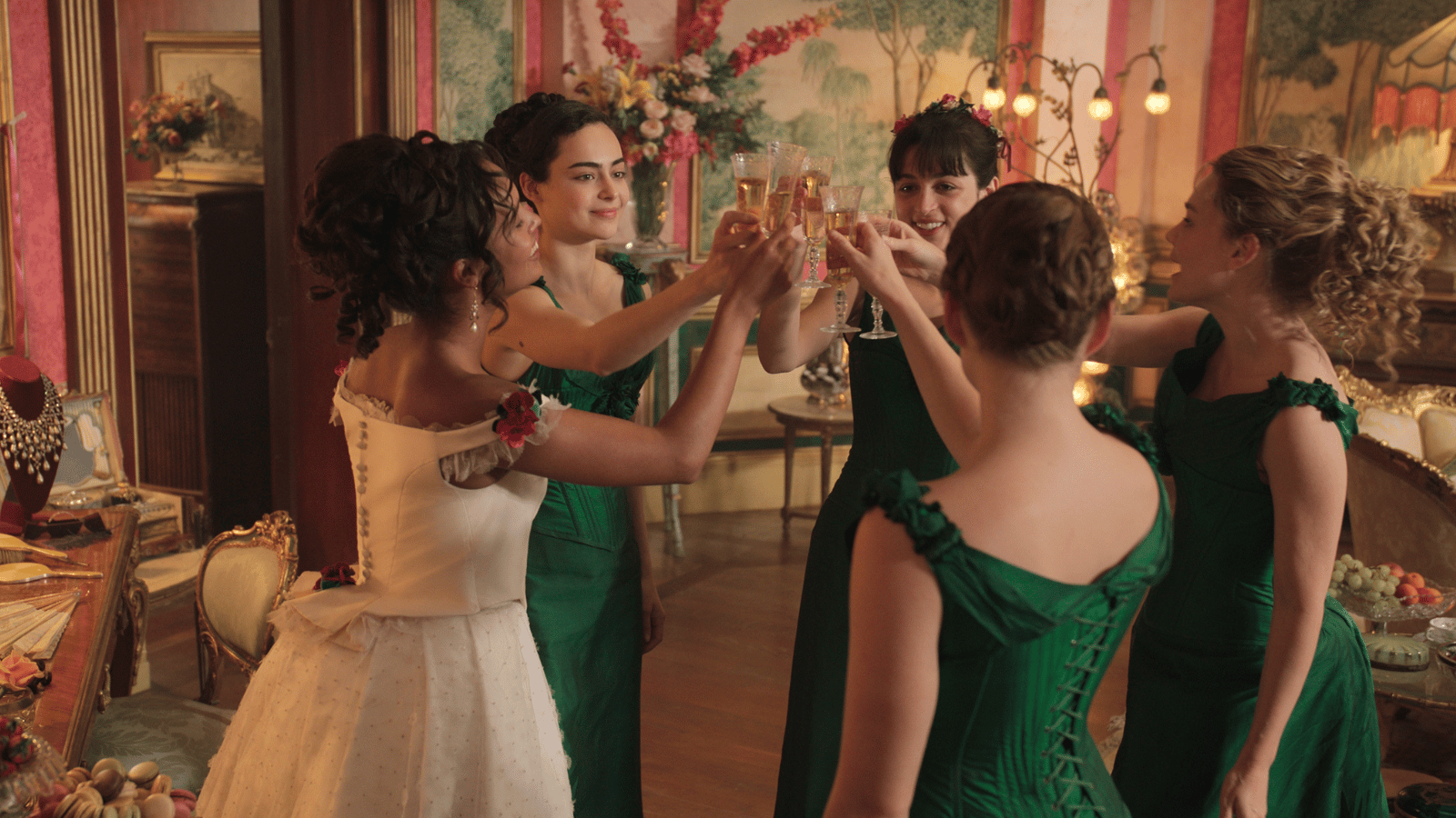 The Buccaneers still. Five women in 1870s formal dresses toasting champagne glasses in the air.