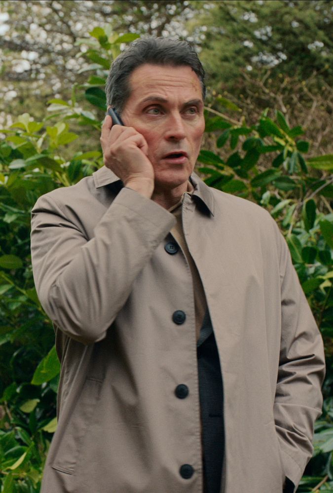 Still from The Diplomat series 2, showing Rufus Sewell standing outdoors on a mobile phone. He wears a long brown jacket.