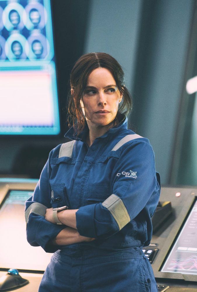 Still from the Rig series 2 showing Emily Hampshire wearing a blue boiler suit, standing in the control room of an oil rig.