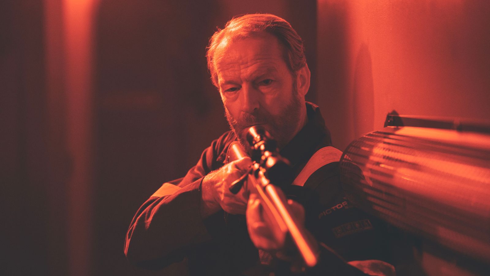 Still from the Rig season 2 showing Iain Glen in a dark room holding up a gun.