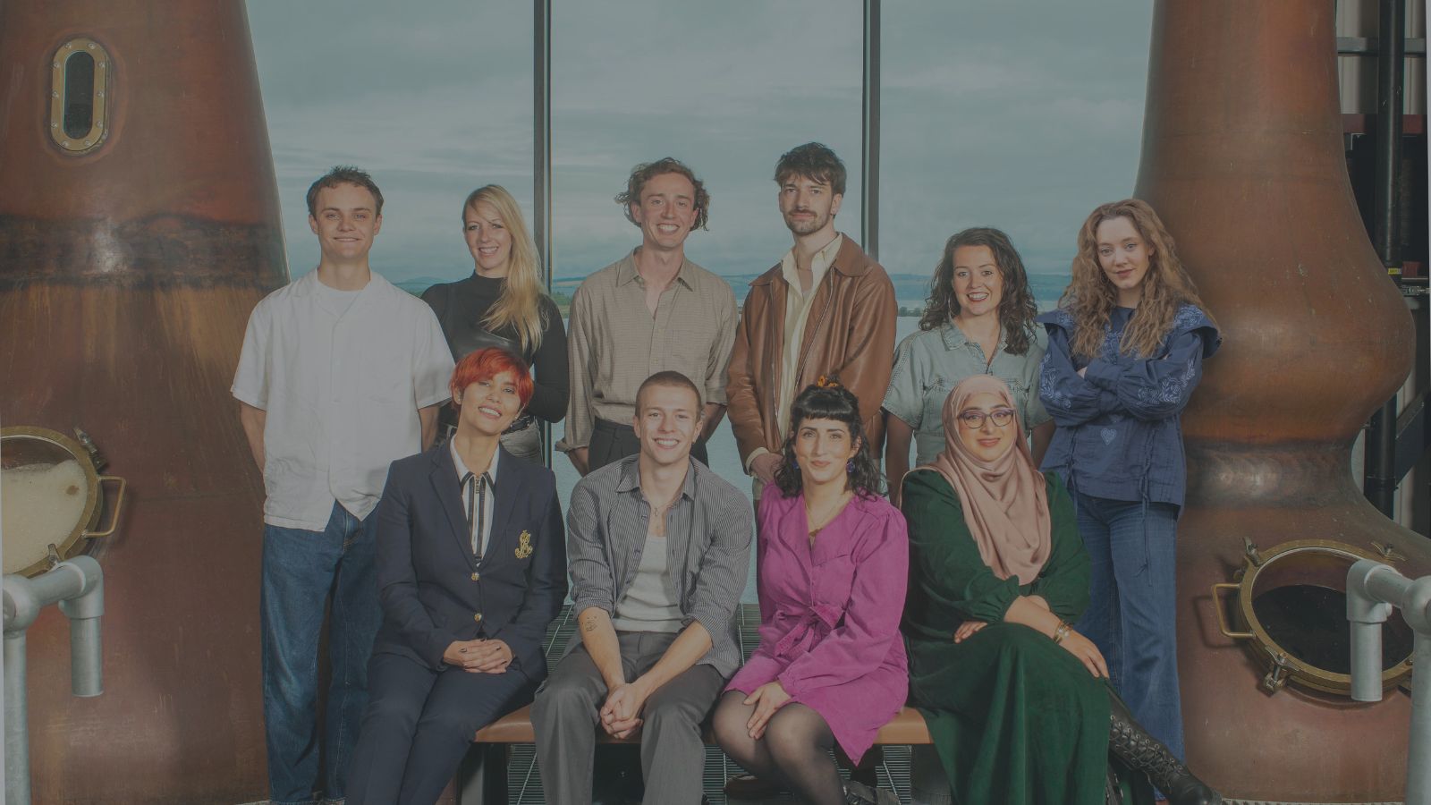 Credit: Rob McDougall/Screen International. The Rising Stars Scotland 2024 cohort are shown in a distillery in two rows. They are Standing (l-r): Séamus McLean Ross (actor), Simone Smith (writer/director), Jamie Fraser (writer/director), Sean Lìonadh (writer/director), Anna Russell-Martin (actor), Mirren Mack (actor)  Sitting (l-r): Nadira Murray (producer), Ruaridh Mollica (actor), Maryam Hamidi (writer), Raisah Ahmed (writer/director)