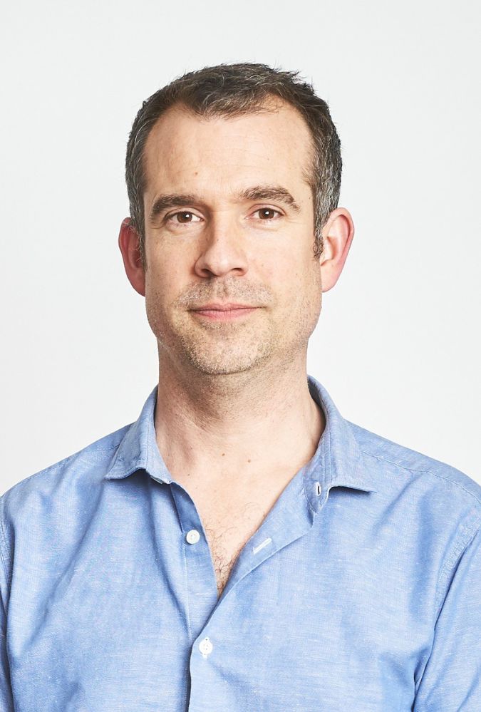 Headshot of Dr Chris van Tulleken, who wears a light blue shirt.