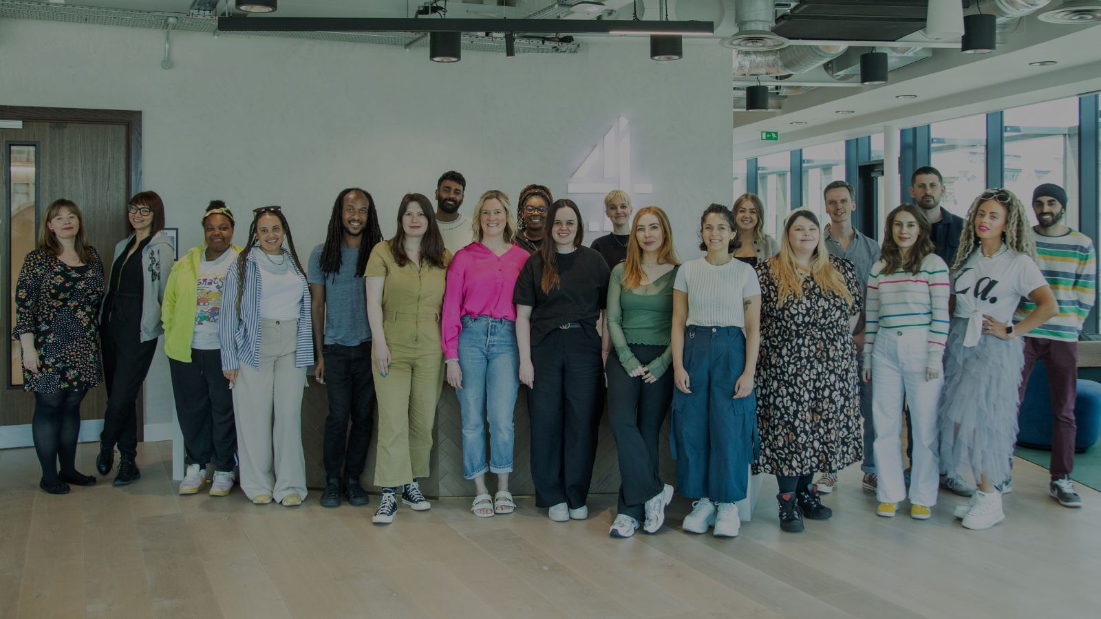 The line up for the C4 New Writers scheme stand in a line in a room, looking at the camera.