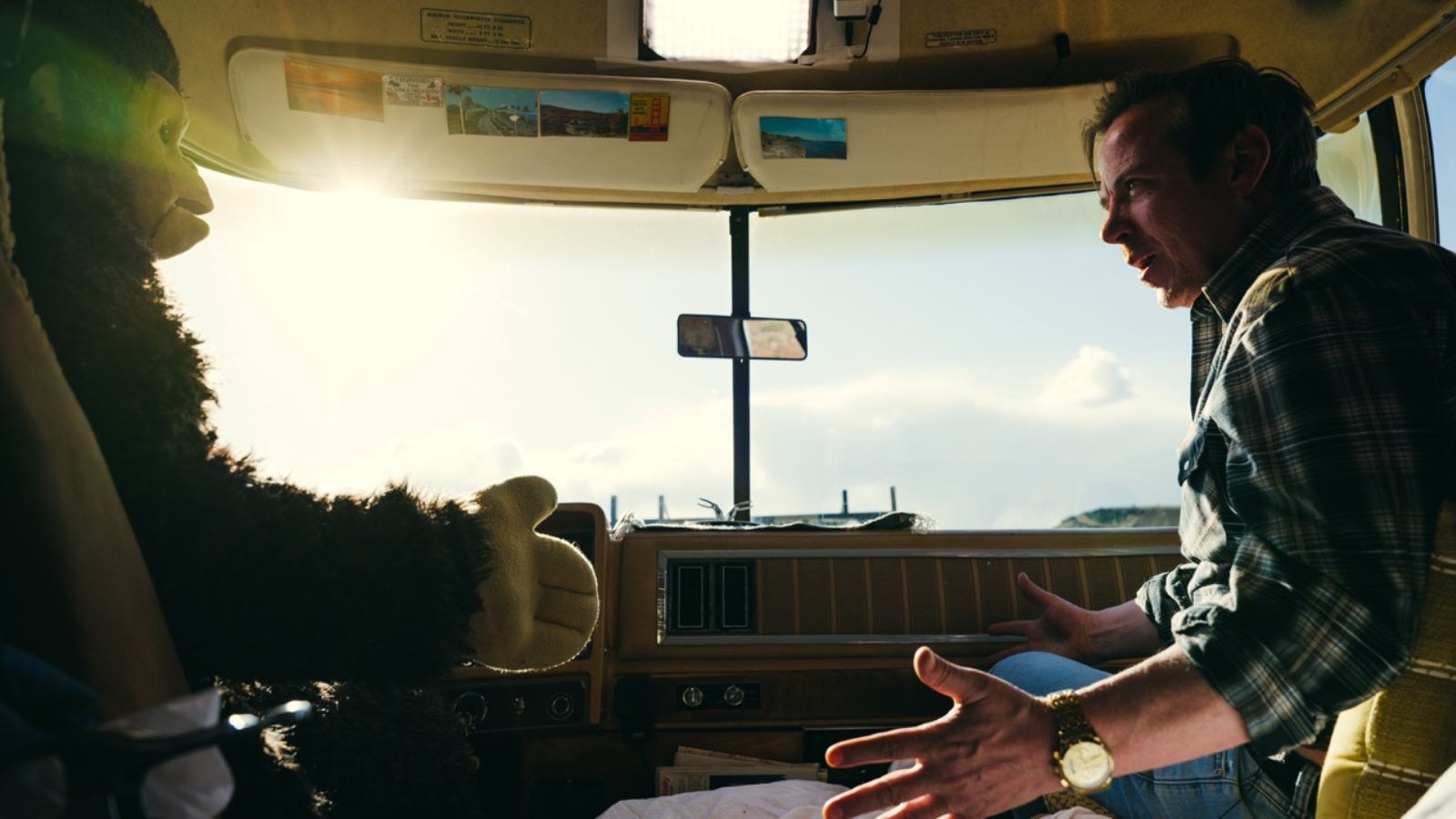 Still from Sunlight, which shows a monkey and a man sitting in the front seats of a camper van. They look at each other in exasperation.