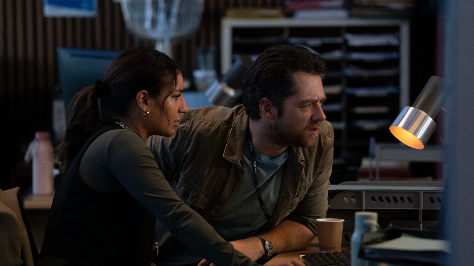 Still from Rebus, courtesy of BBC. Lucie Shorthouse and Richard Rankin as Siobhan Clarke and John Rebus both lean on a desk looking at a computer screen in a room.