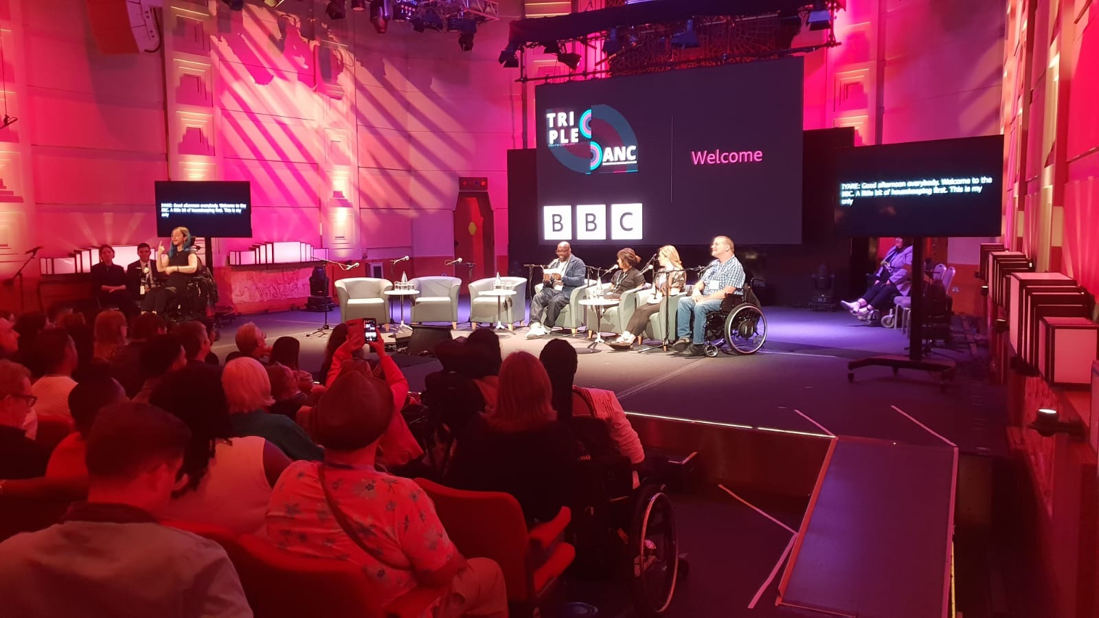 Image from previous TripleC event, which shows a large room with four people sitting at the front, with an audience facing the speakers. A large screen behind the speakers reads TripleC DANC, welcome, and has the BBC logo.