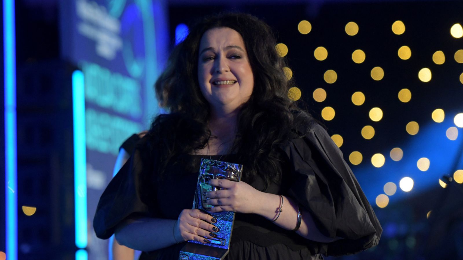 Ashley Storrie leaves the stage at the BAFTA Scotland Awards with her award. She wears a black dress.