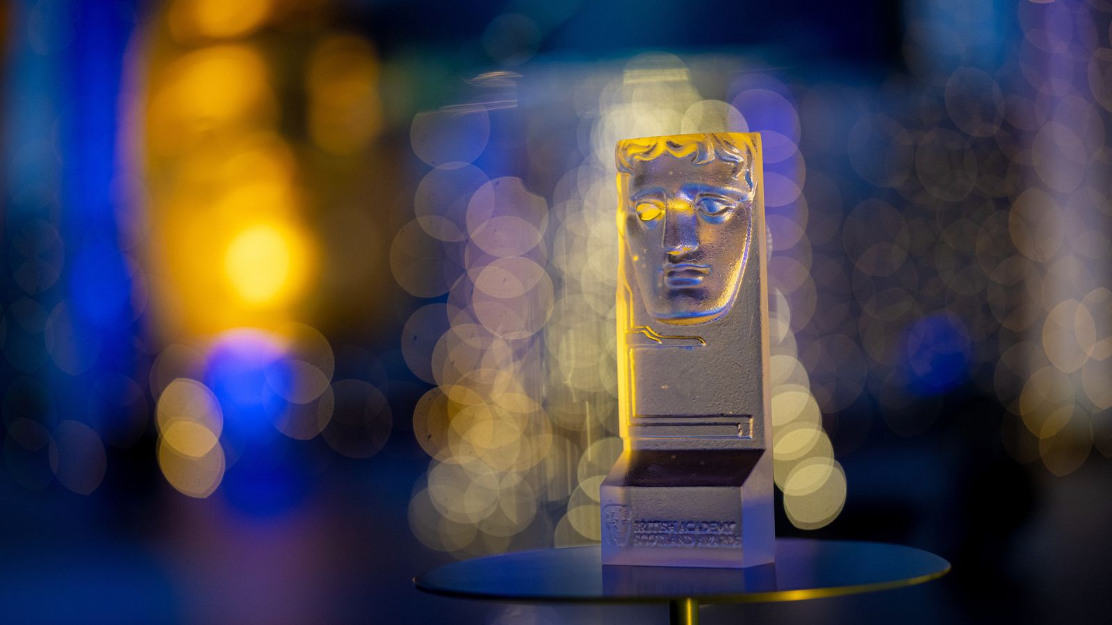 A BAFTA award sits on a table against a blue and gold hazy background.