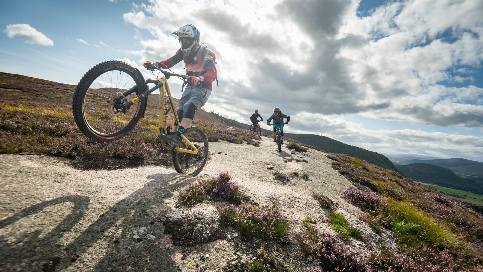 Three mountain bikers ride down a trail outdoors on a sunny day.