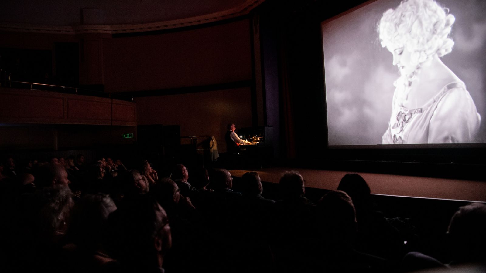 Image shows an audience watching a black and white film in a cinema screen