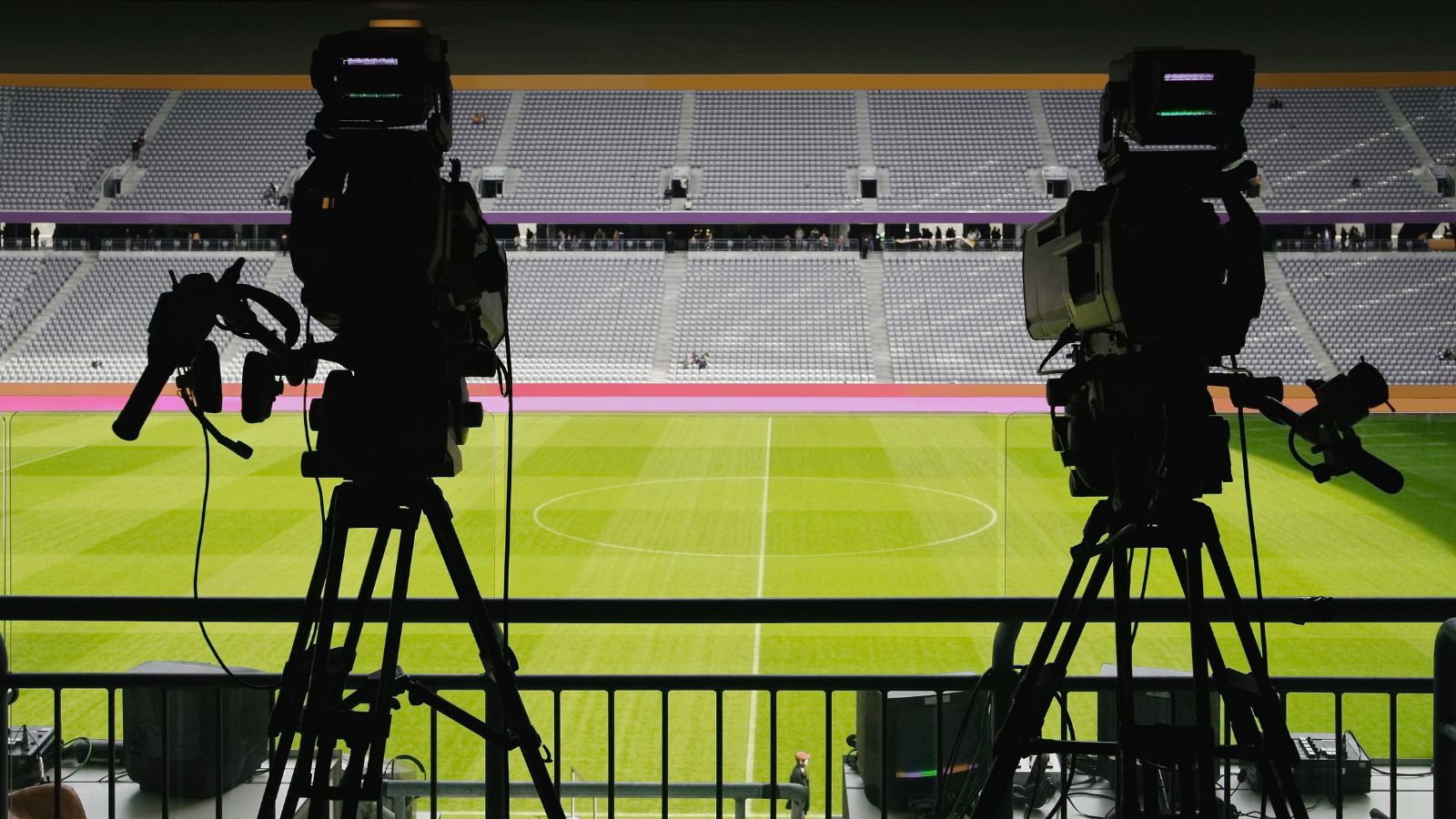 Two cameras on tripods are shown facing towards the pitch at a football stadium.